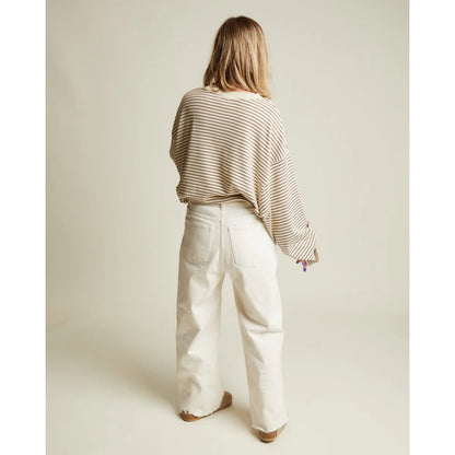 Eine frau trägt ein lockeres erwachsenen lenni coco stripe langarmshirt in beige und schwarz mit weißen denim-hosen