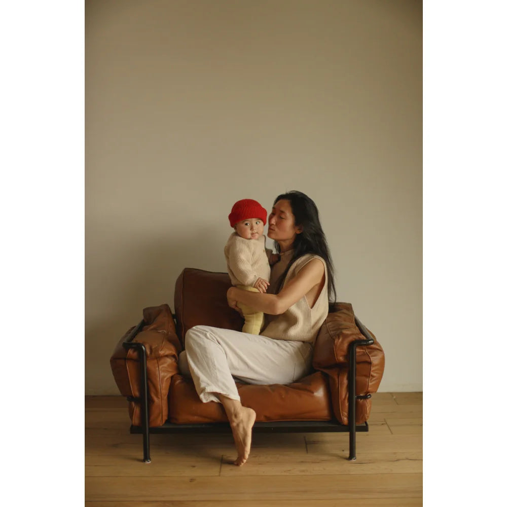 Mama hält Baby in braunem Ledersessel, trägt den Adult Vest Helle Cream