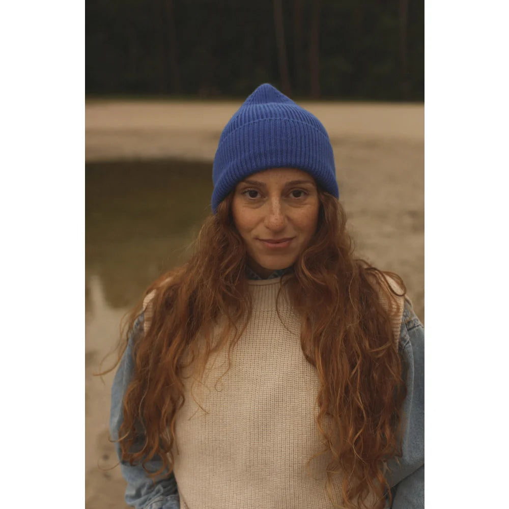 Frau mit langen roten Wellenhaaren, blauer Mütze und cremfarbenem Weste über Jeansjacke