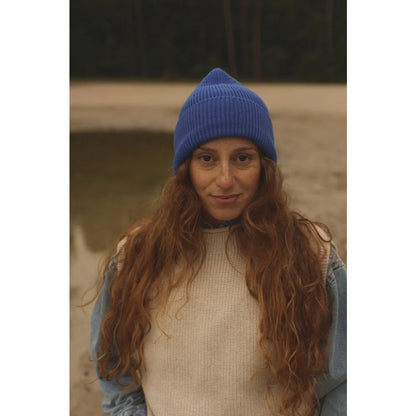 Frau mit langen roten Wellenhaaren, blauer Mütze und cremfarbenem Weste über Jeansjacke