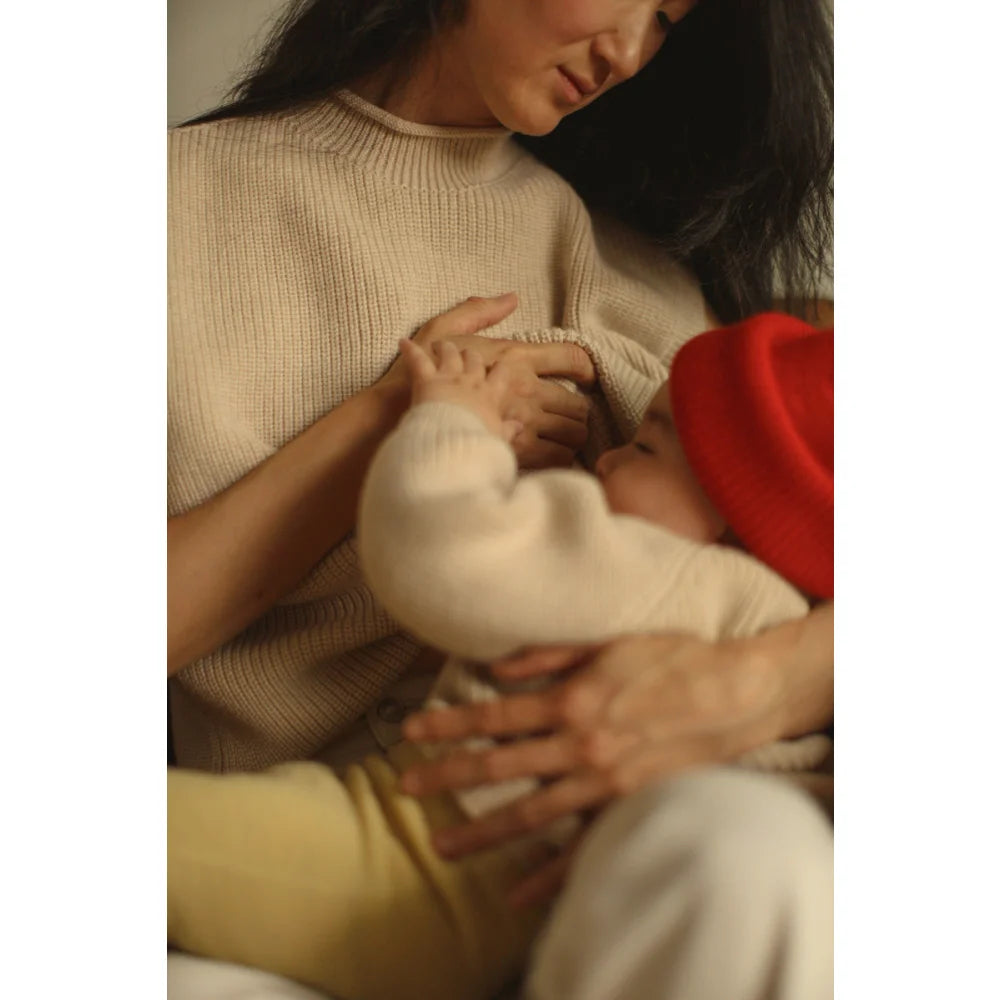 Mama hält Baby mit rotem Hut, passend zum Adult Vest Helle Cream Produkt