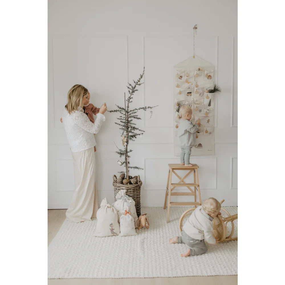 Familie schmückt einen schlichten Weihnachtsbaum mit dem Adventskalender mit gestickten Illustrationen