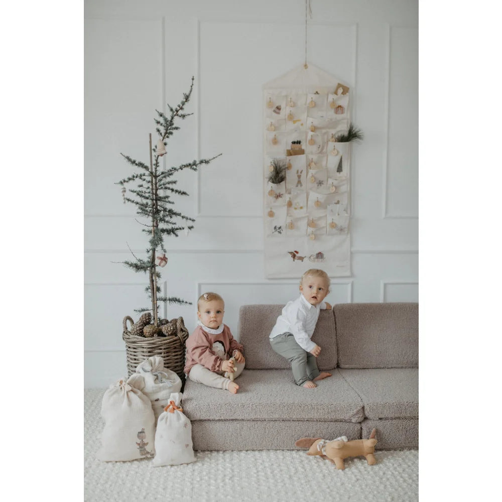 Zwei Kinder auf einem modularen Sofa mit Weihnachtsdeko und dem Adventskalender mit gestickten Illustrationen