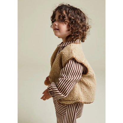 Kind kuschelt in sandfarbenem Amos Folk Gilet über gestreiftem Pyjama