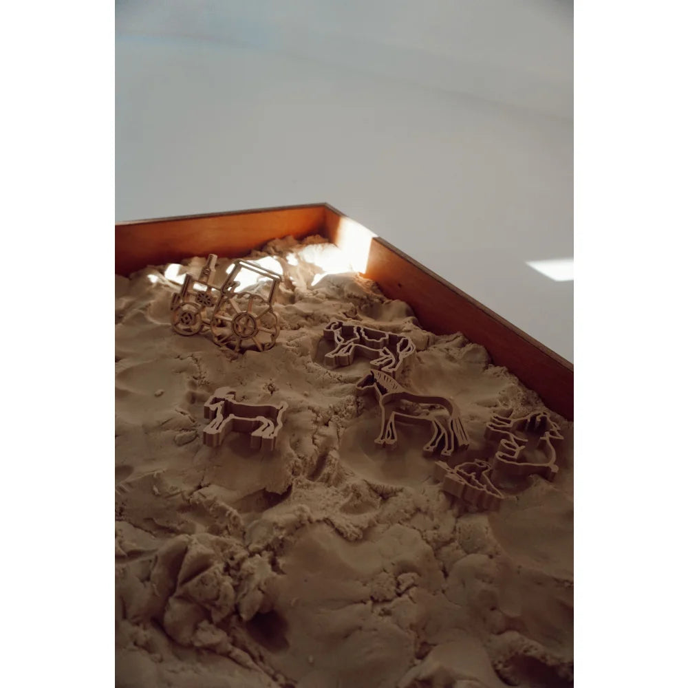 Tierförmige Ausstechformen und eine kleine Holzkarre im Sand für Kinderbacken