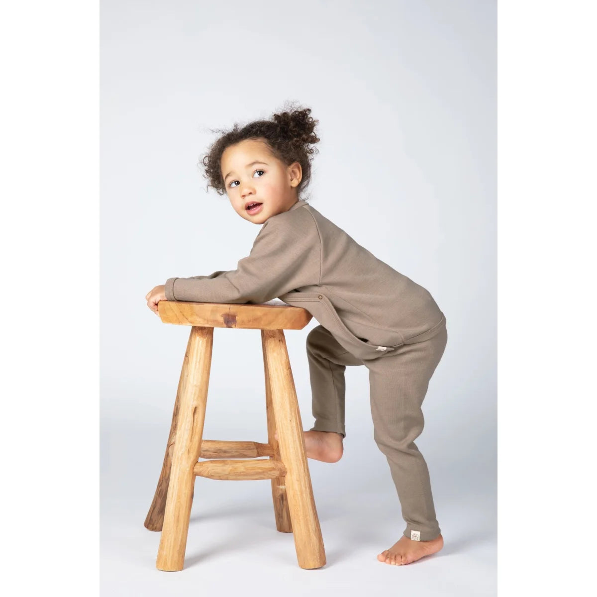 Baby in sandfarbenem Langarm-Jumpsuit mit Knöpfen und Bündchen