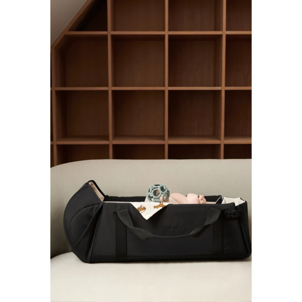 Schwarze Baby-Nest Amber Oat mit kleinem Kind und Spielzeug im Reisebett