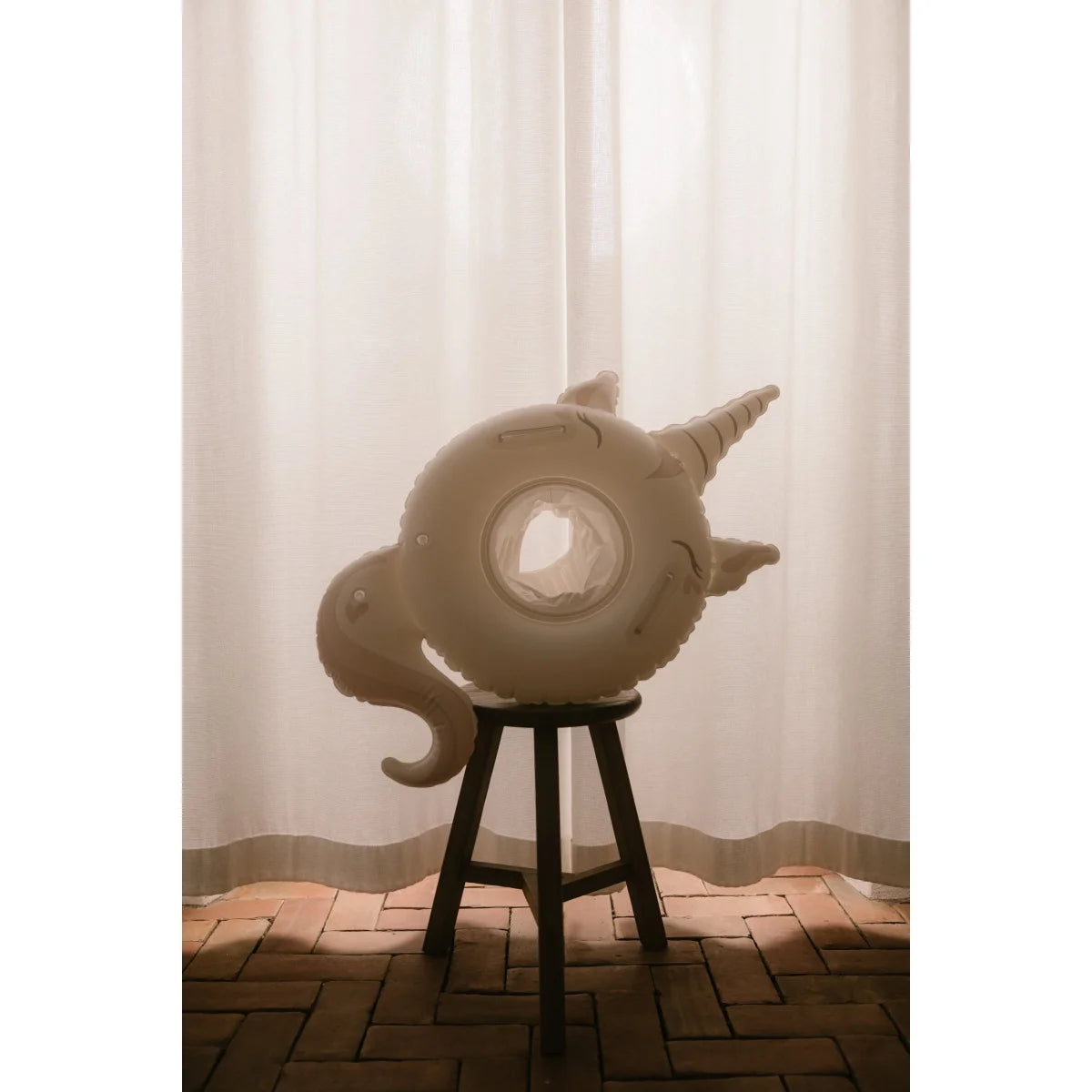 Baby-schwimmring sweet unicorn in off-white mit spirale horn und lockigem schwanz auf dunklem holzhocker für ökologische baby- & kinderprodukte