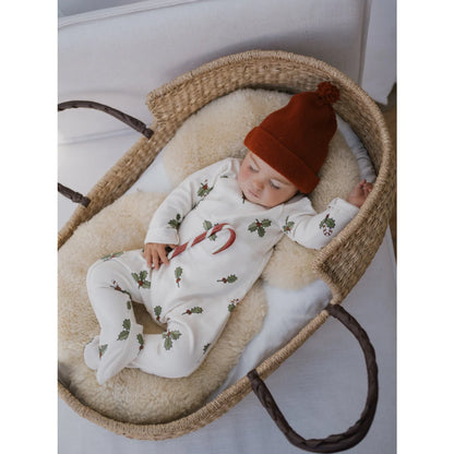 Baby in weißem Schlafsack mit Stechpalmen und Zuckerstange, orange Strickmütze