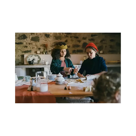 Zwei junge frauen mit goldener krone und orangefarbener mütze sitzen an einem holztisch mit bakes backzutaten
