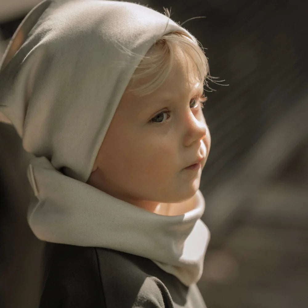 Kind eines Kindes mit hellfarbener Mütze und Halswärmer in Ecru