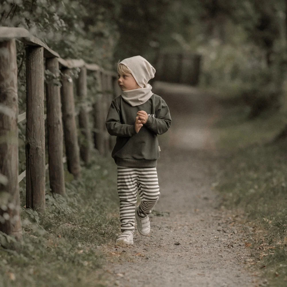 Kind eines Kindes in grüner Langarmshirt, gestreiften Hosen, Ecru Beanie und Halswärmer