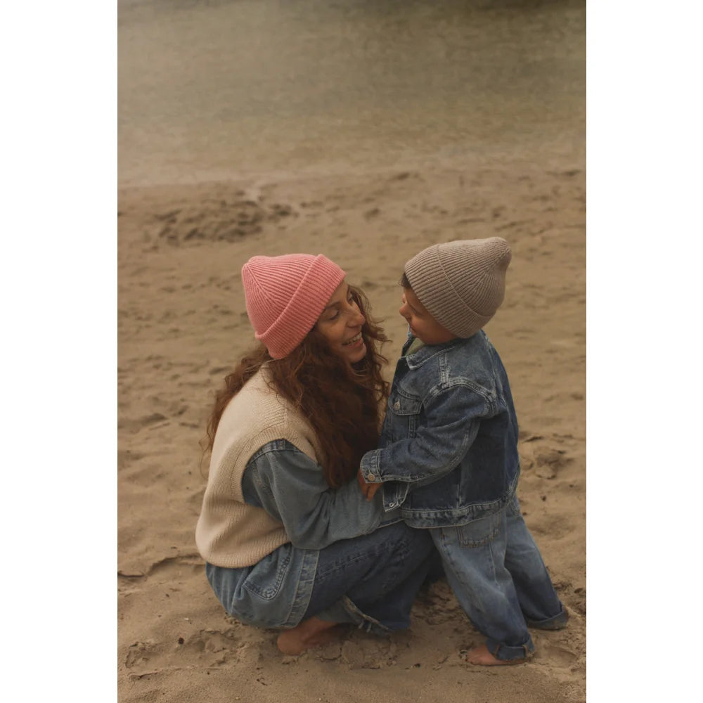 Zärtlicher Moment zwischen Elternteil und Kind in passenden Strickmützen am Strand