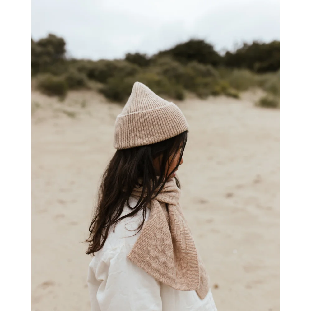 Person in Beanie Fonzie Sand and light clothing enjoying a sunny beach day