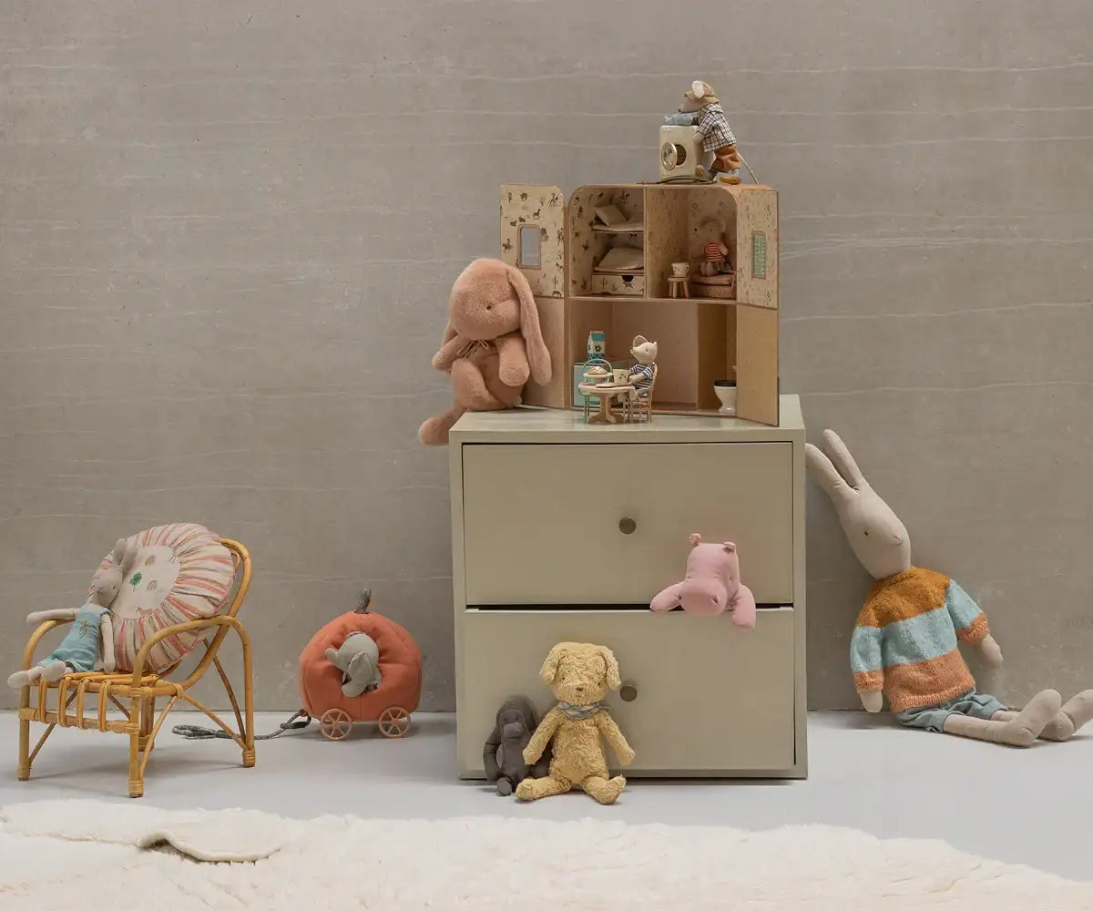 Beige Kommode mit zwei Schubladen, Holzknöpfen und weichen Pastell-Plüschtieren, die darum herum kuscheln.