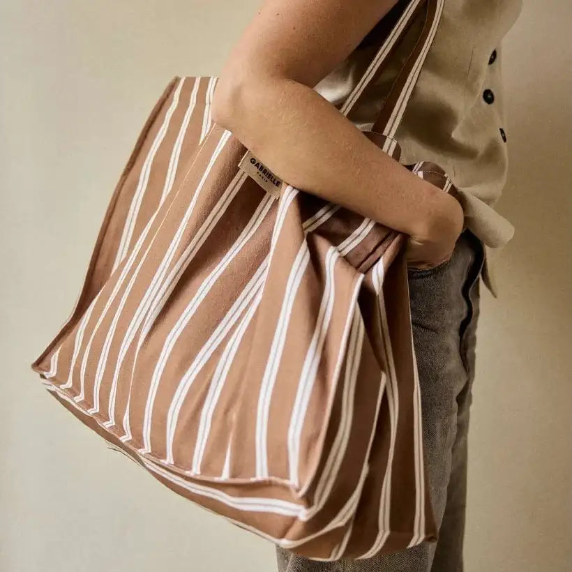 Eine beige und weiße vertikal gestreifte Canvas-Totebag mit sichtbarem Markenanhänger.