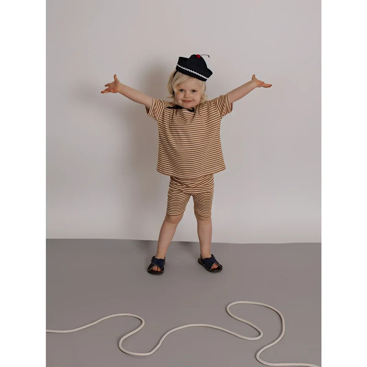 Kind in Biker Shorts Copper Stripes, gestreift braun-beige, marineblauer Hut