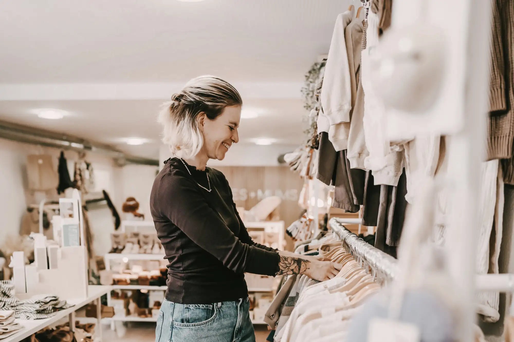 Frau mit blonden Haaren, die Kleidung an einem Ständer in einem Boutique durchstöbert
