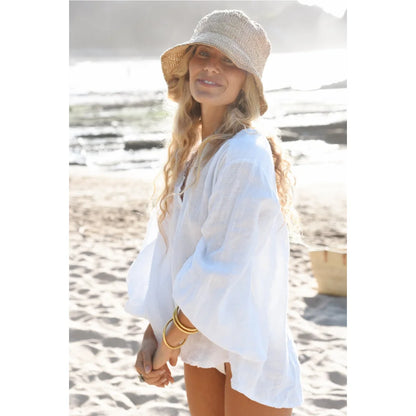 Frau in weißer Leinenbluse und Strohhut am Strand für Bluse Lily Blanco