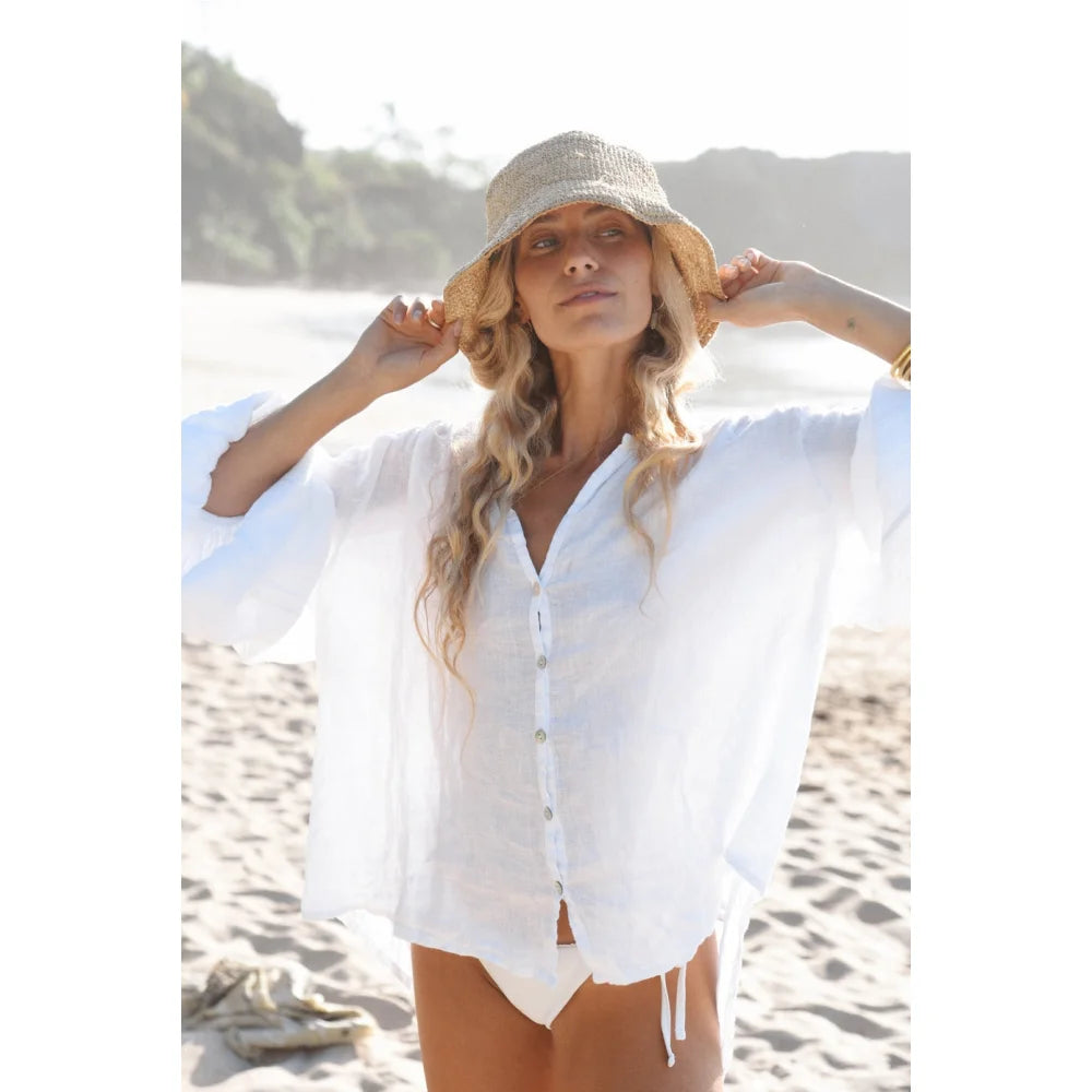Frau trägt weiße Leinenbluse Lily und Strohhut im Produkt Blanco