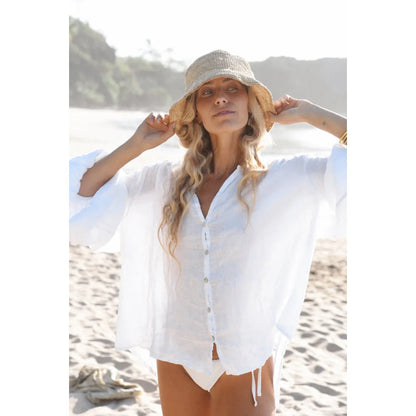 Frau trägt weiße Leinenbluse Lily und Strohhut im Produkt Blanco