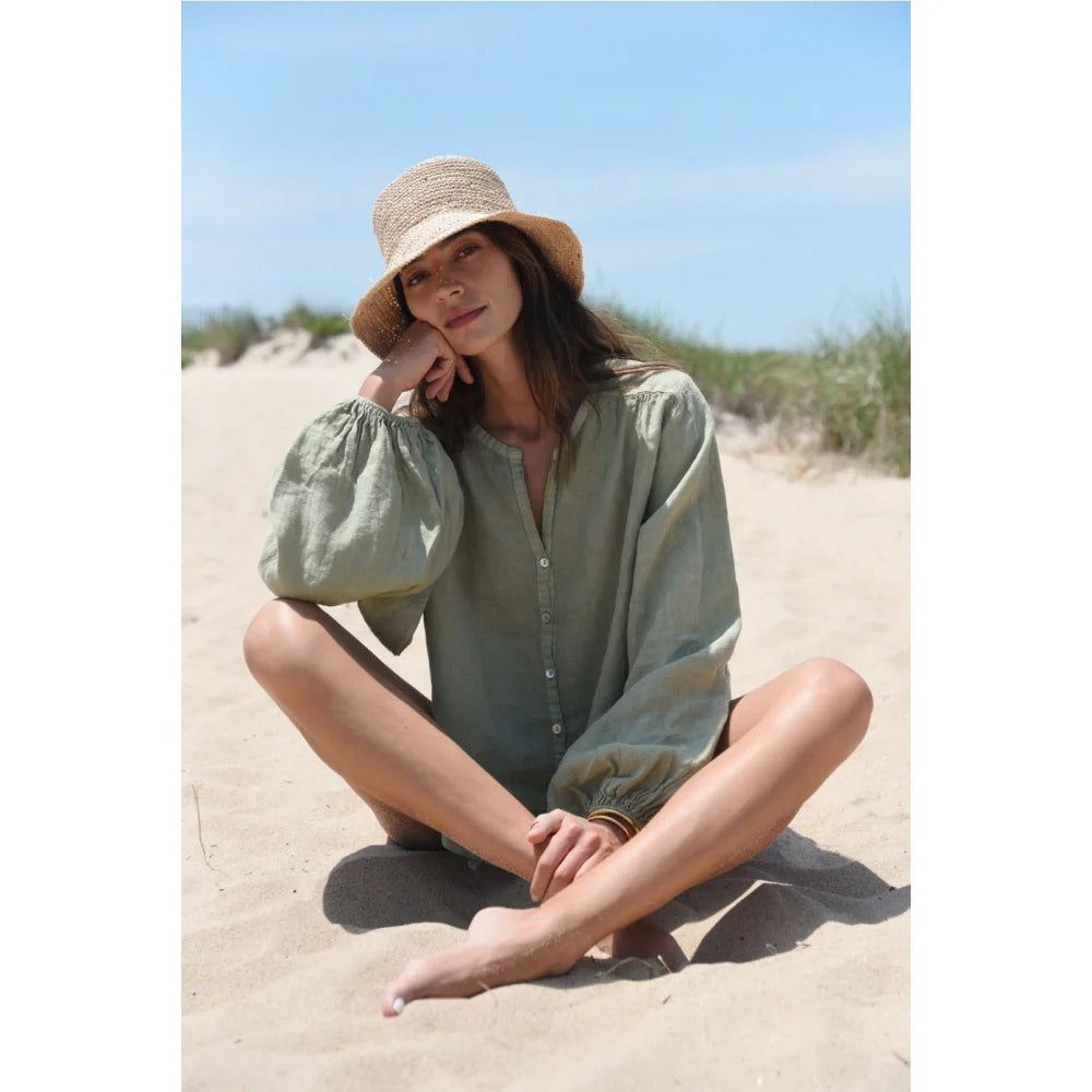 Frau trägt Sage Bluse Lily mit voluminösen Ärmeln und Strohhut