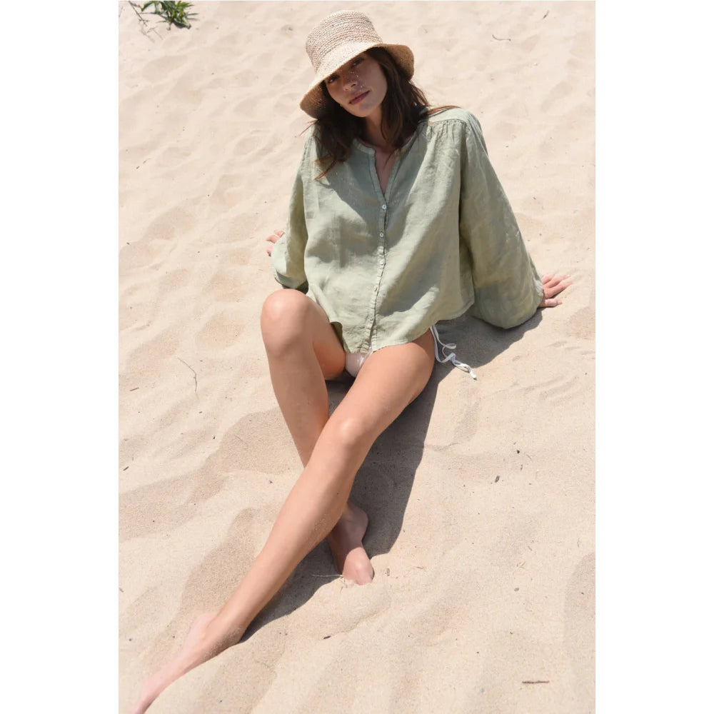 Frau in hellgrüner Bluse Lily Sage mit Strohhut am Strand sitzend