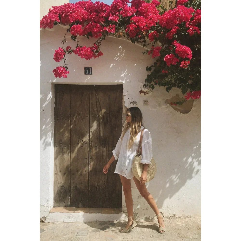 Frau in weißem Outfit steht an einer Tür mit pinken Bougainvillea-Blüten