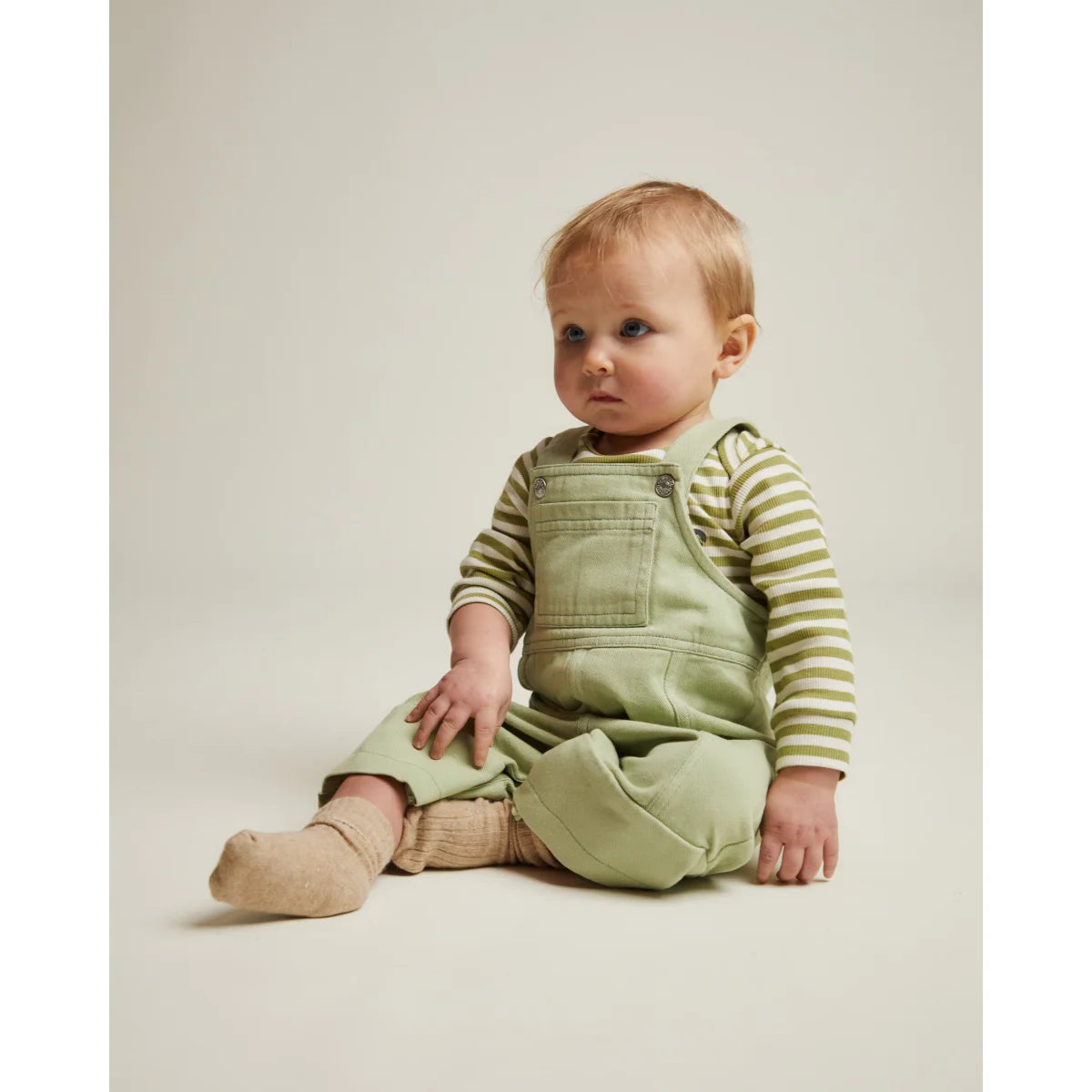 Ein baby trägt mintfarbene denim-blythe dungarees mit gestreiftem langarmshirt aus weichem stoff