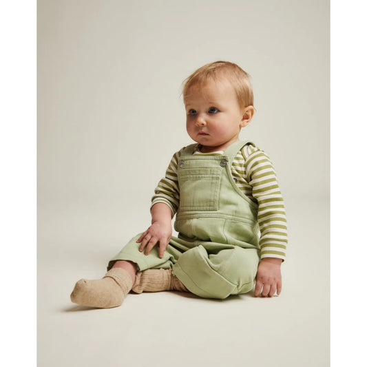 Ein baby trägt mintfarbene denim-blythe dungarees mit gestreiftem langarmshirt aus weichem stoff