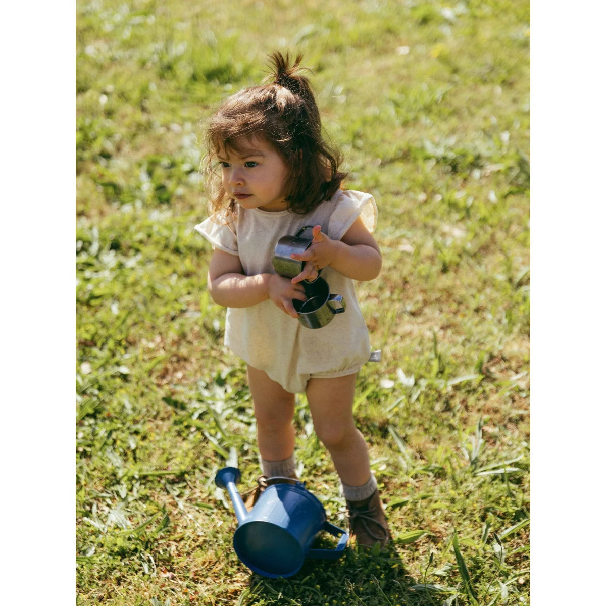 Kind hält zwei glänzende Gießkannen bei floralem Print Ribbed Body