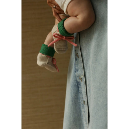 Baby trägt cremefarbene Merino Booties mit grünem Bändchen
