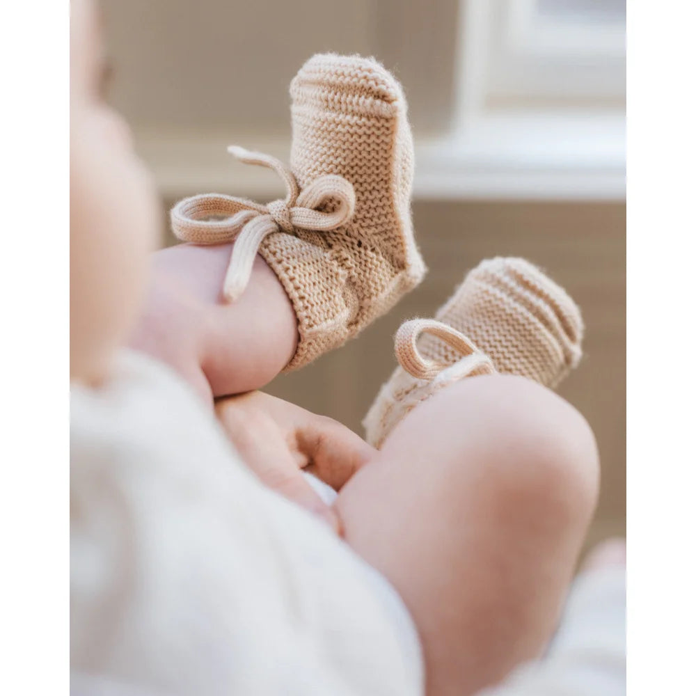 Beige Strick-Babybooties mit Ribbonschnürung an kleinen Füßen, Produkt: Booties | Oat