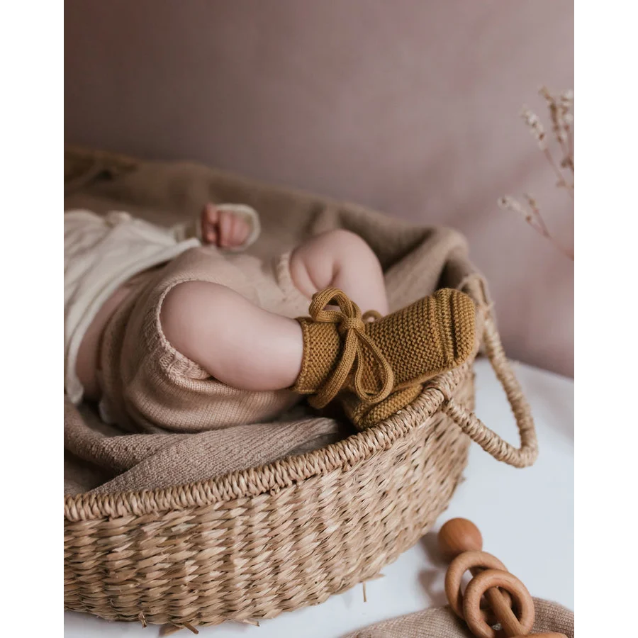 Neugeborenes Baby mit gestrickten Booties im gewebten Korb, Booties in Ocker