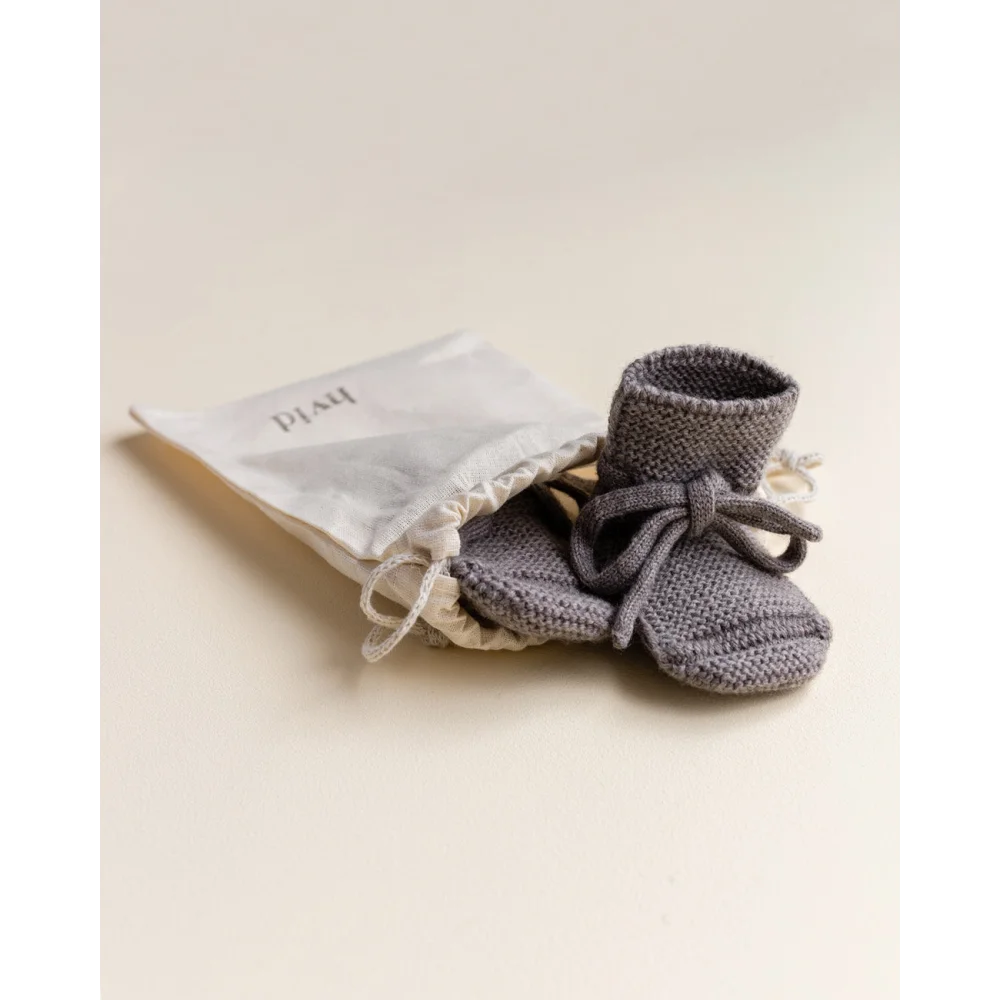 Grau gestrickte Babybooties mit Schleifen, begleitet von einem kleinen Stoffbeutel