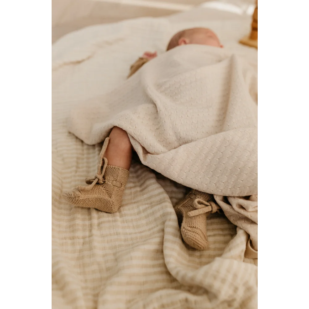 Neugeborenes Baby in weißer Decke mit gestrickten beigen Stiefeln