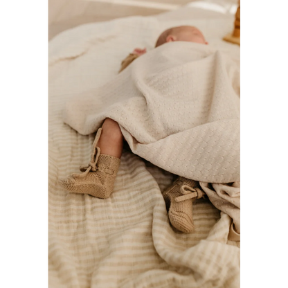 Neugeborenes Baby in weißer Decke mit gestrickten beigen Stiefeln