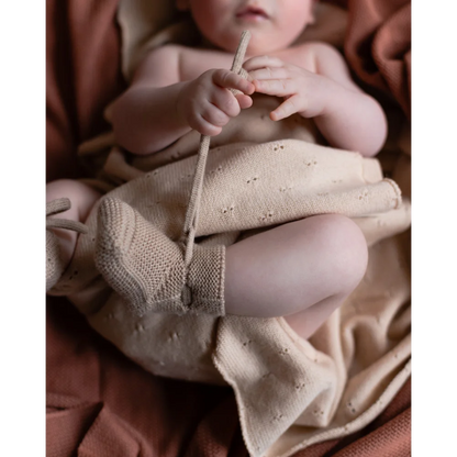 Baby mit gestrickten Sand-Booties hält einen Holzstock oder Spielzeug