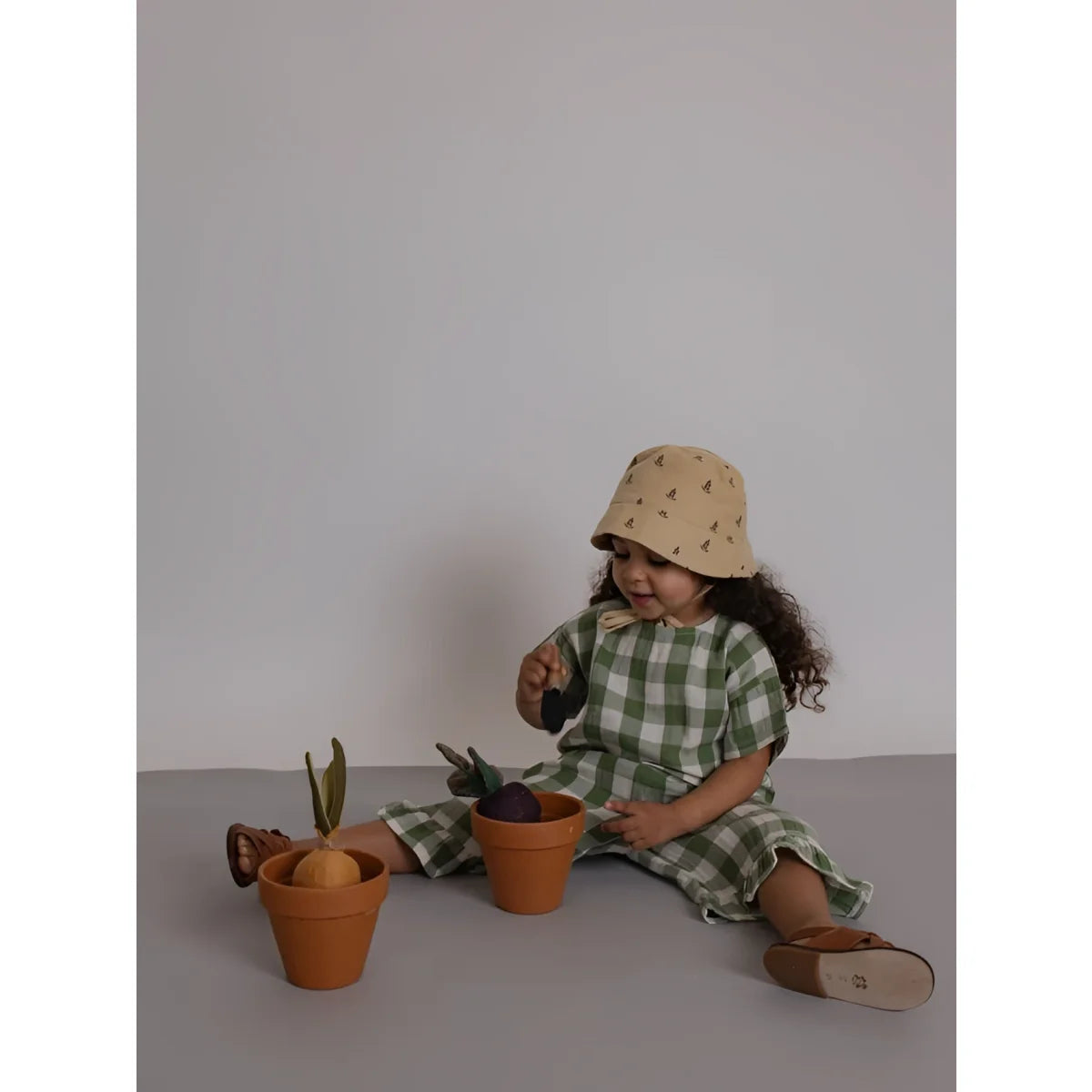 Kleinkind in Dill-Gingham Boxy T-Shirt sitzt mit Töpfen auf Boden