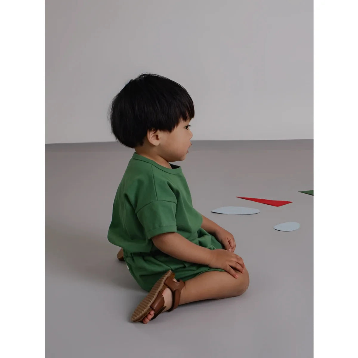Kind trägt eine seagrass grüne boxy t-shirt mit kurzarm und braunen sandalen