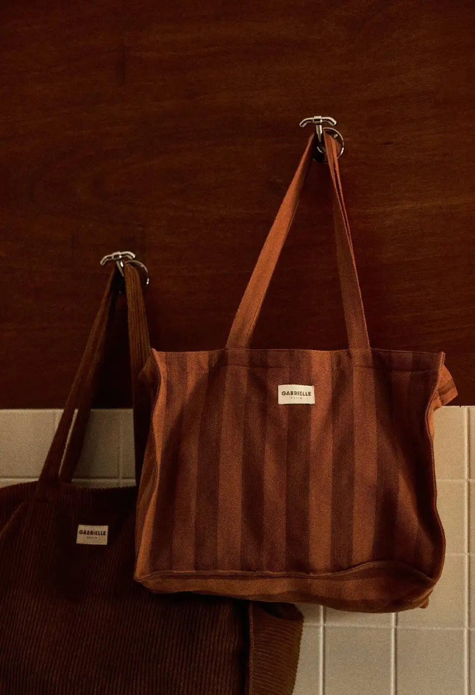Braune Cordtasche mit vertikalen Streifen und einem weißen Label mit der Aufschrift „gabrielle“ auf der Vorderseite.