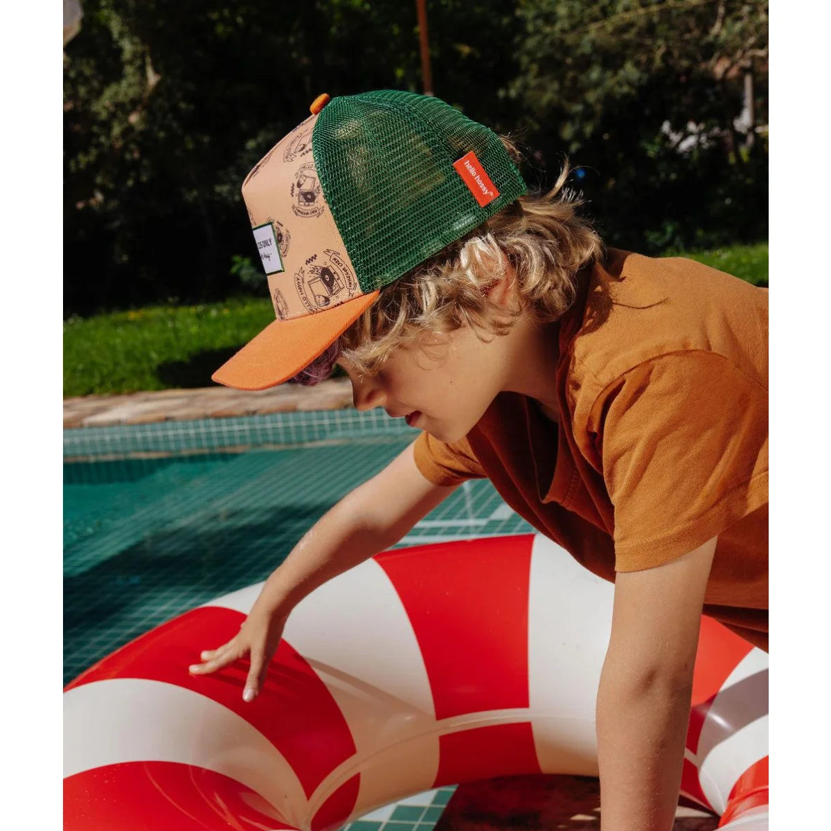 Ein kind trägt eine grüne mesh trucker cap mit orangefarbenem schirm und beige panelen mit schwarzen logos von inkee