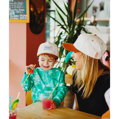 Ein kind trägt die cap mini beige mit orangefarbenem schirm und einem kleinen rechteckigen patch vorne