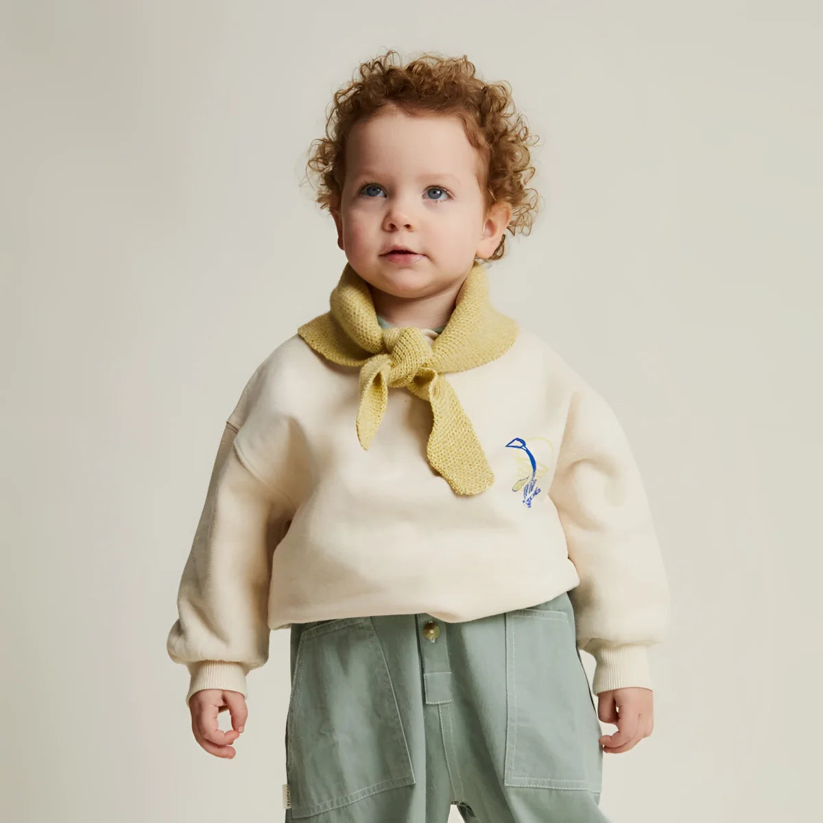 Cremfarbener strickpullover carner grow slowly mit senfgelbem strickschal und blauem vogelstick auf der brust