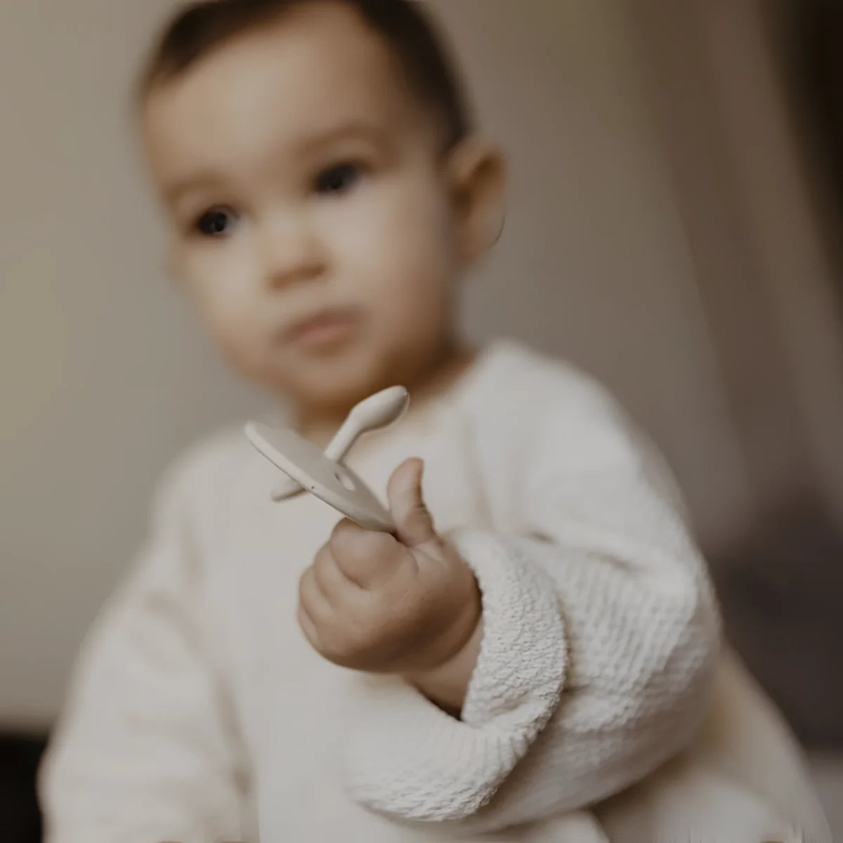 Baby hält weißes Spielzeugflugzeug ChooChoo Schnuller 0-6 Monate Sand