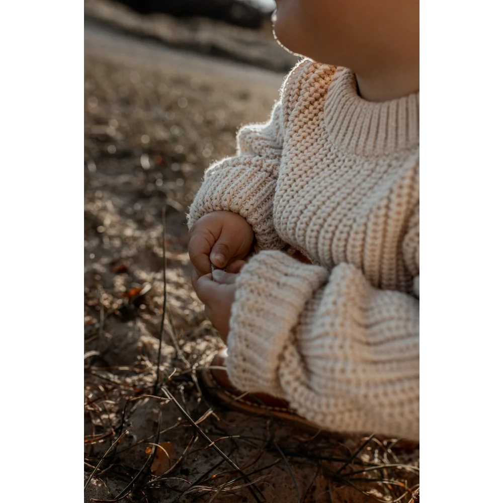 Kindliches Kind trägt cremigen, grob gestrickten Pullover auf dem Boden sitzend