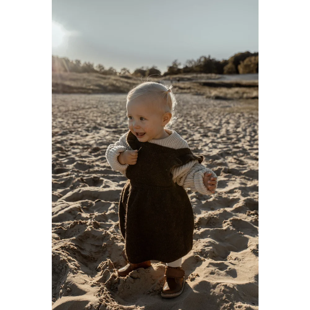 Lächelndes Baby in dunklem Outfit auf einem Sandstrand, Chunky Knit Sweater Oat