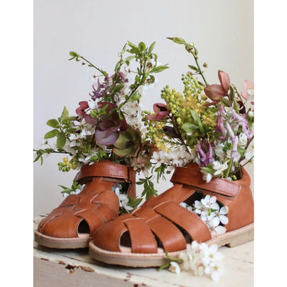 Klassische cognacfarbene sandalen aus braunem leder mit geflochtenen riemen und weicher sohle gefüllt mit weißen lila und grünen blumen