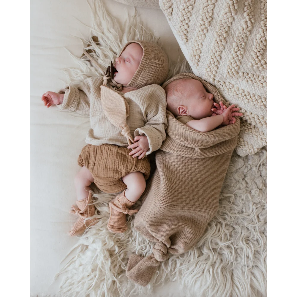 Neugeborenes Baby schläft friedlich in gemütlicher Strickkleidung auf Cocoon Babydecke Sand