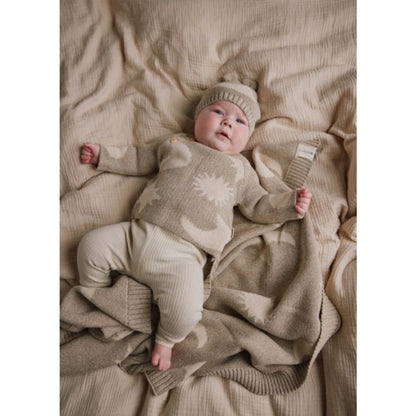 Baby in weichem Beige-Strickoutfit mit weißen Mond-Stern-Mustern auf passender Decke